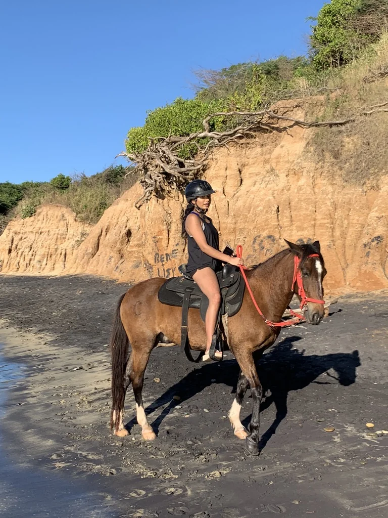 I am horseback riding on a black-sand coastal beach
